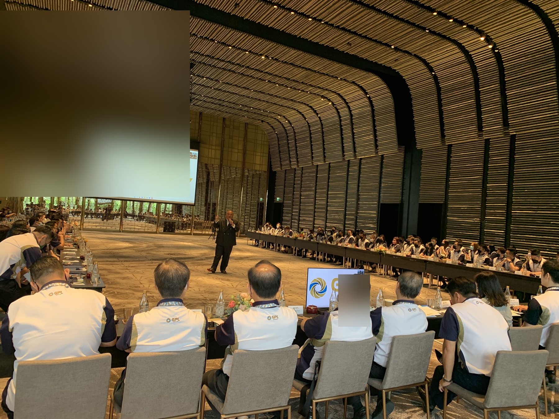 Scale shot — both table rows stretching back, Marcus at the floor presenting